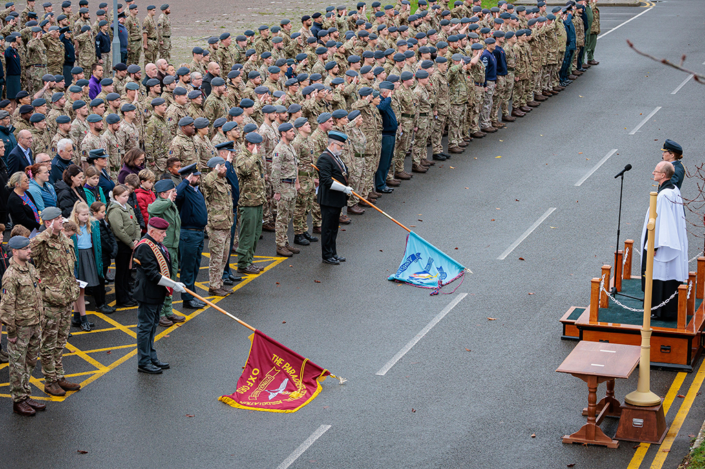 The congregation of Station personnel and some families, standing together as the bugler plays the Last Post and Standards are lowered to the ground.